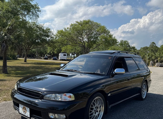 A 1996 Subaru Legacy Wagon GT-B in black, parked outdoors, showcasing its sleek, elongated body with sporty side skirts and factory alloy wheels.