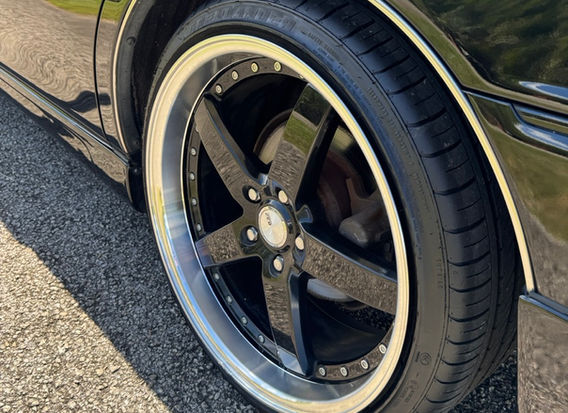 Side profile of 1999 Toyota Crown Majesta 3.0 black sedan featuring aftermarket coilovers, black interior seat covers, and 19-inch alloy wheels – low mileage luxury JDM import
