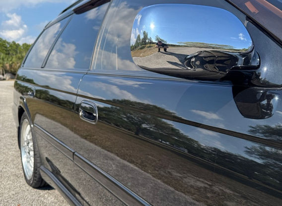 A 1996 Subaru Legacy Wagon GT-B in black, parked outdoors, showcasing its sleek, elongated body with sporty side skirts and factory alloy wheels.