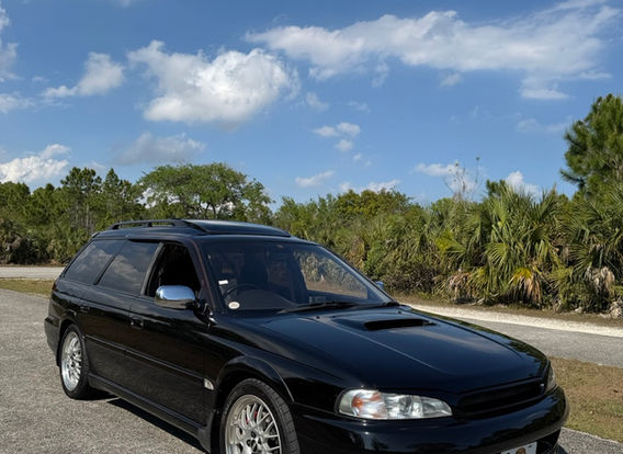 A 1996 Subaru Legacy Wagon GT-B in black, parked outdoors, showcasing its sleek, elongated body with sporty side skirts and factory alloy wheels.