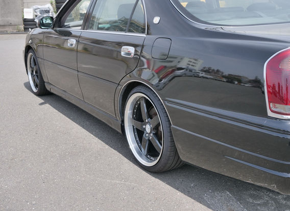 Side profile of 1999 Toyota Crown Majesta 3.0 black sedan featuring aftermarket coilovers, black interior seat covers, and 19-inch alloy wheels – low mileage luxury JDM import