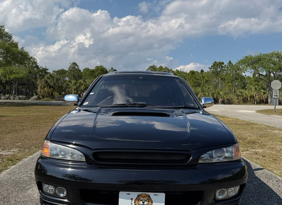 The front fascia of a 1996 Subaru Legacy Wagon GT-B, featuring its signature twin-turbo hood scoop, rectangular headlights, and a bold Subaru grille.