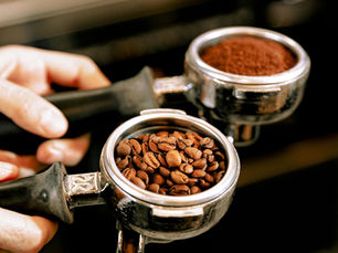 Barista holding an espresso portafilter filled with fresh coffee beans next to a portafilter with ground coffee at a Nashville coffee shop