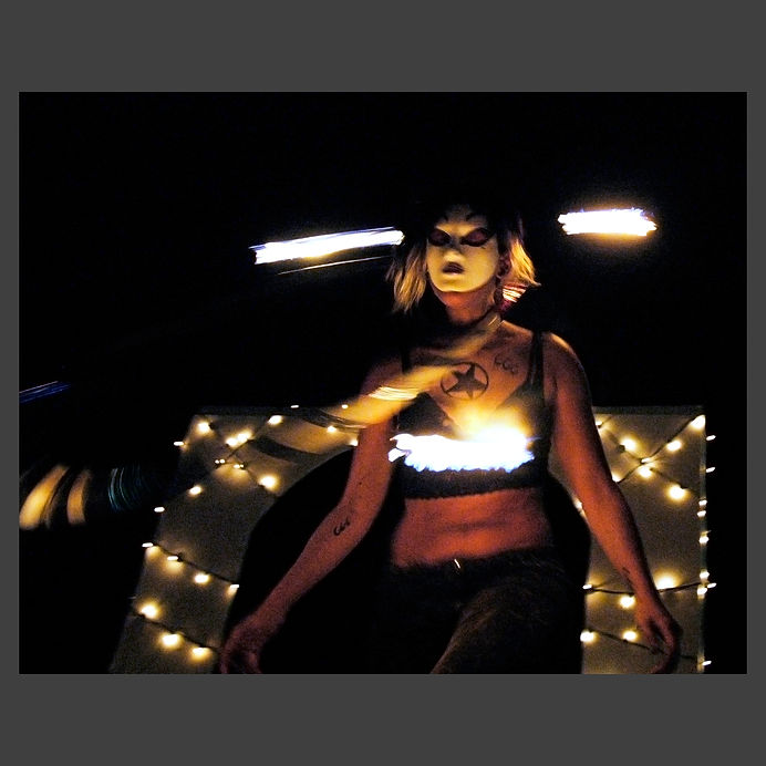 fire dancer with a white mask spinning a fire hoop around her neck