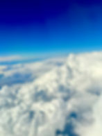 Shades of white fluffy clouds above land that is brown and green 