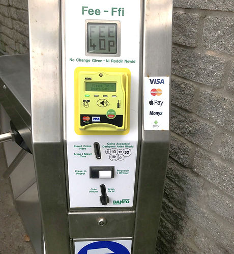 Fee-Ffi pay-and-display payment terminal with contactless card reader, coin slot, and directional arrow beside a turnstile