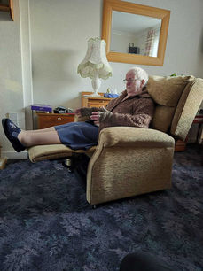 Elderly man relaxing in a recliner, feet up, holding device