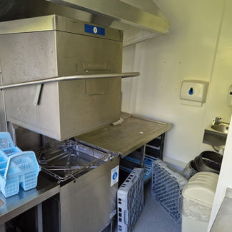 Commercial kitchen with a large stainless steel dishwasher, blue dish racks, and stacks of plates