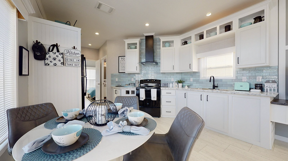 Interior look at a cozy park model kitchen with euro style vent hood over the range, soft teal ceramic tile backsplash, white shaker style cabinetry, and a 42" round dining room table that seats 4.