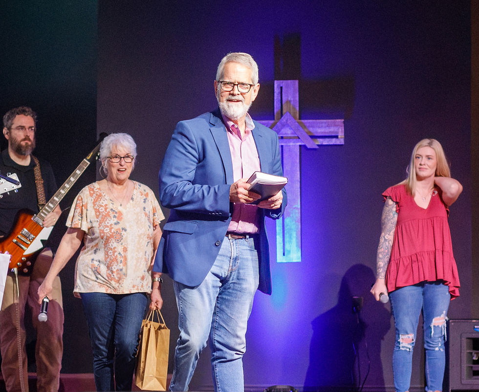 Tracy Reynolds holding a Bible and smiling on stage with worship team and band behind him at Grace Fellowship Madison