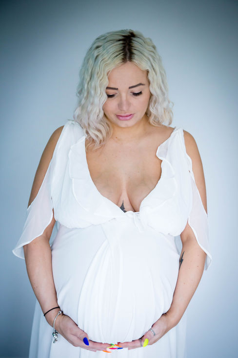 Maternity photo of mother in a white dress naturally cradling bump at home in Essex