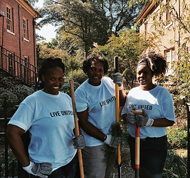 Three volunteers holding gardening tools and smiling.