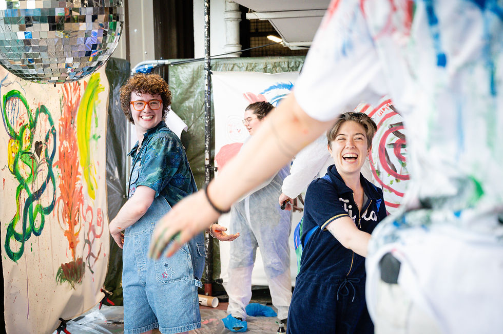 People smiling outside in front of painted canvas. They're smiling and twisting their arms in a big stretch.
