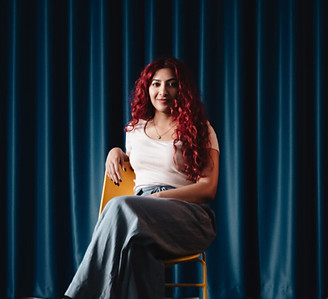 image of a person with red hair sat confidently in front of blue curtains