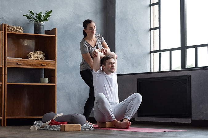 Man doing shoulders stretching, yoga exerise. Female teacher helping him to stretch muscle