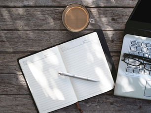 Glasses on a floral notebook next to a green hat on a textured gray fabric. Reflective lens hints at a calm, stylish atmosphere.