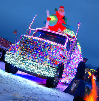 A semi-truck fully decorated with glowing Christmas lights at the Belgrade, Montana Christmas Village, featuring a festive inflatable Santa Claus in a biplane mounted on the roof.