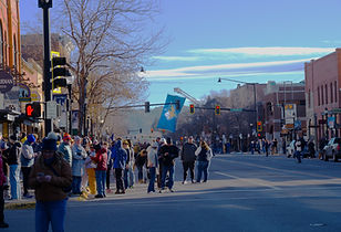 Wide-angle view of Main Street in downtown Bozeman, Montana, during the 2025 MSU Bobcats National Championship parade, featuring crowds of fans and a large Bobcats logo banner flying in the distance.