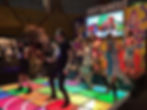 People dance energetically on a colorful, illuminated floor at a "Just Dance 2016" event. A bright screen displays game visuals.