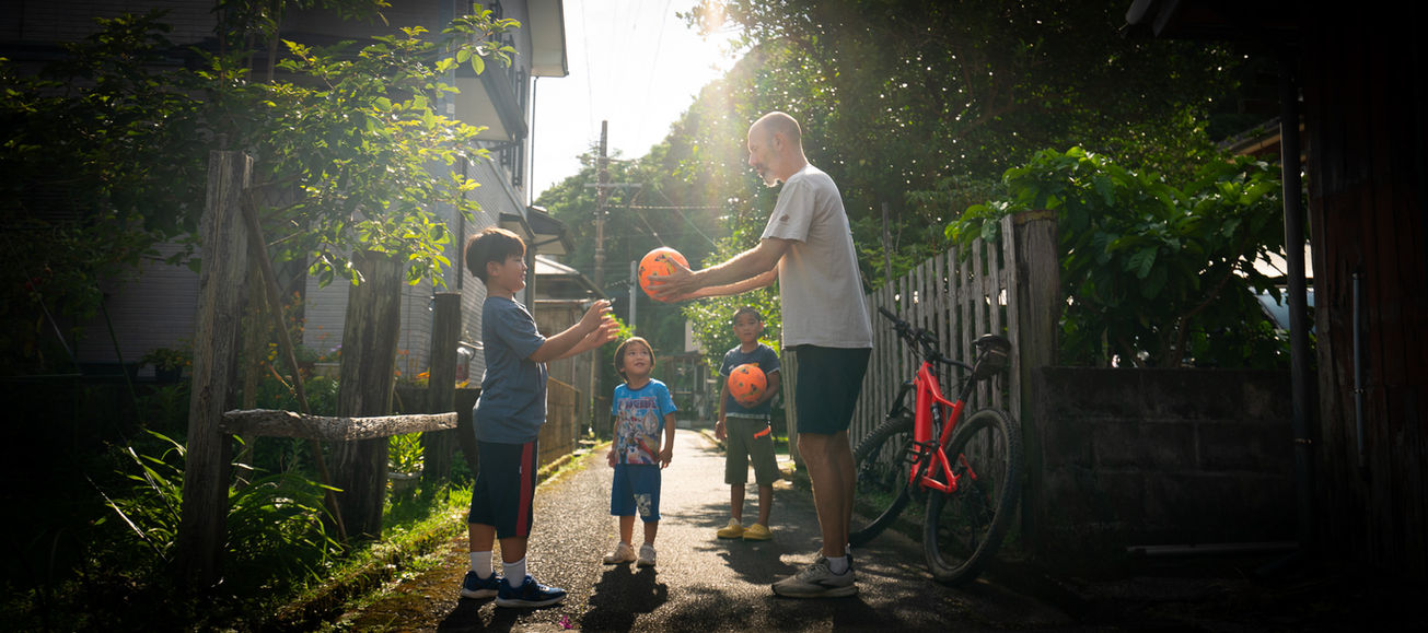 夕暮れの村で自転車に乗り子供へボールを渡す