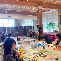 Participants creating collages and mixed-media artwork together around a large table during a Heartistry workshop.