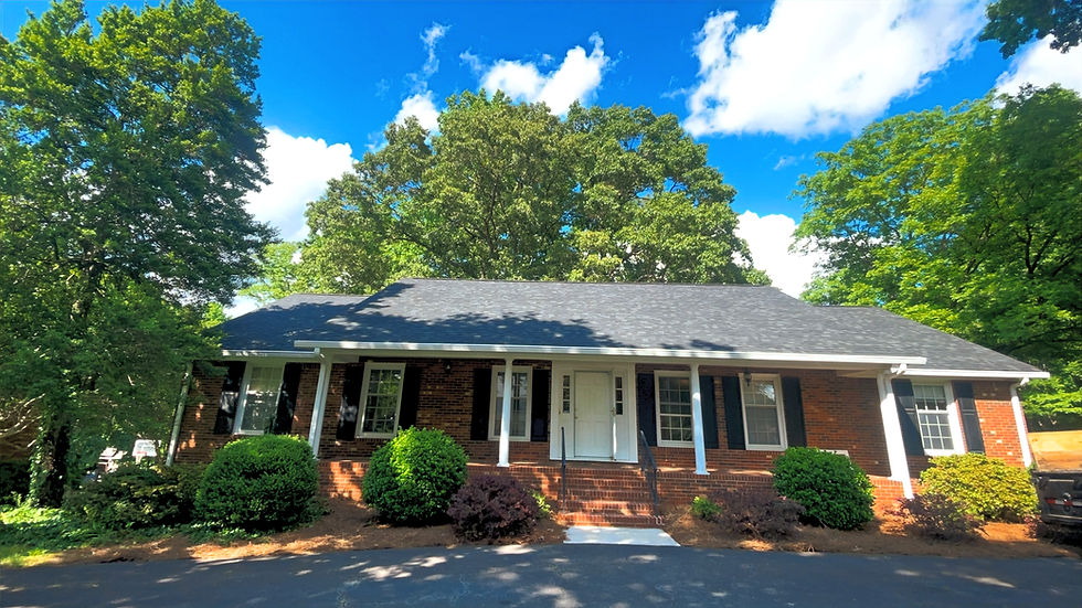 One-story brick home with a porch and green trees.