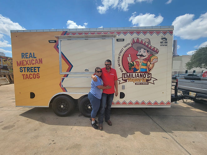 Couple who owns a Food Trailer Standing in front of their food trailer