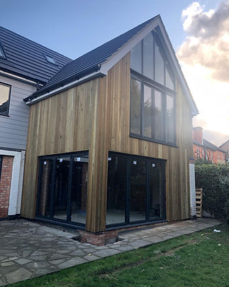 Tall wooden house extension with a black roof and black frame french doors.