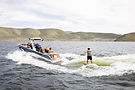 Blue malibu surf boat on Deer Creek pulling a surfer behind it on a surf board.
