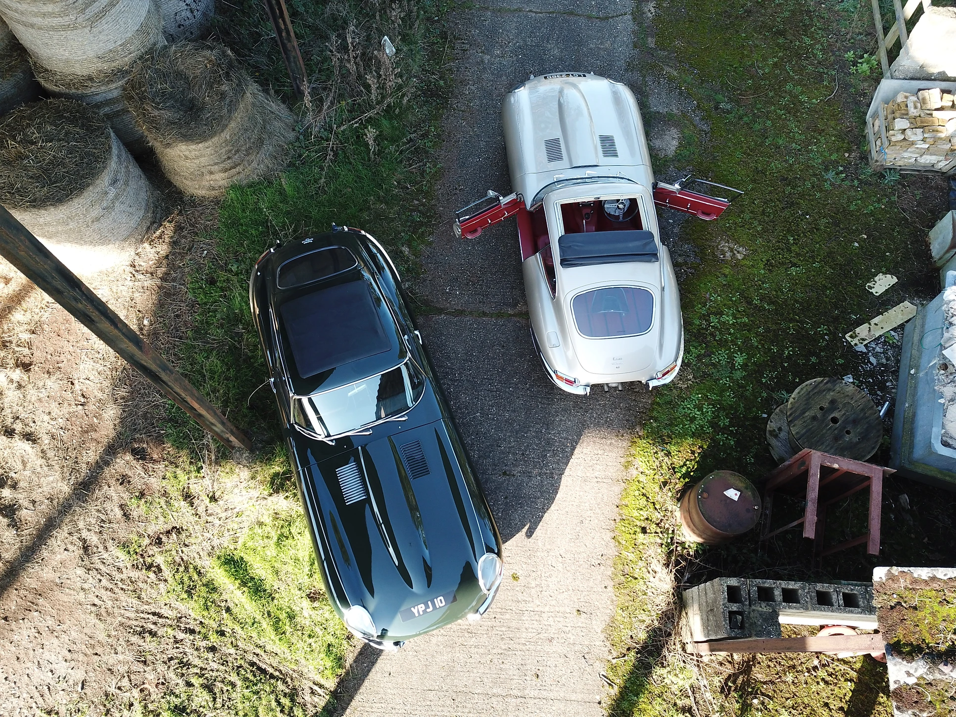 2 Jaguar e-types parked next to eachother at a barn yard.