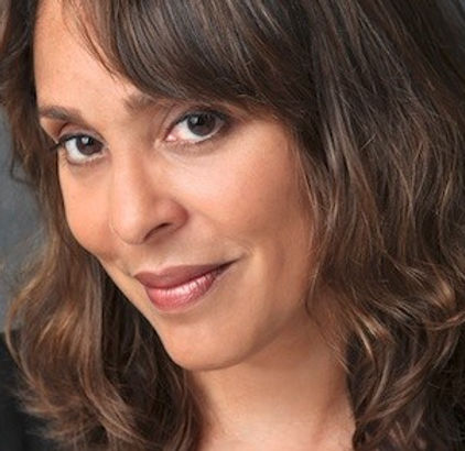 (Image Description: A portrait photograph of Natasha Trethewey from the shoulders up. Natasha is wearing a black blazer and below-the-shoulder wavy light brown hair. She has a small, closed-mouth smile on her face. Behind Natasha is a smoky gray-colored photography background.)