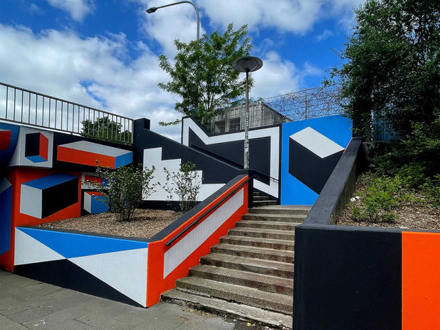 Meta-Sattler-Straße, Treppenaufgang
Fortführung des 700 qm Wandbilds in der Unterführung der Meta-Sattler-Straße. Der Treppenaufgang wurde mit großflächigen Farbflächen und klaren Linien minimalistisch neu gefasst. Architektur und Grafik reagieren miteinander – Licht, Schatten und Perspektive erzeugen eine stille räumliche Fiktion.