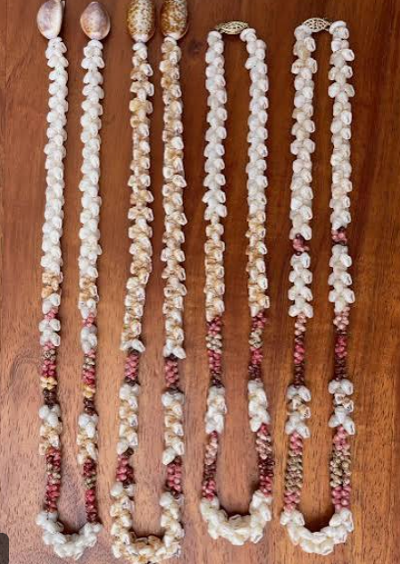 Several white and pink shell necklaces laid out vertically on a wooden surface.