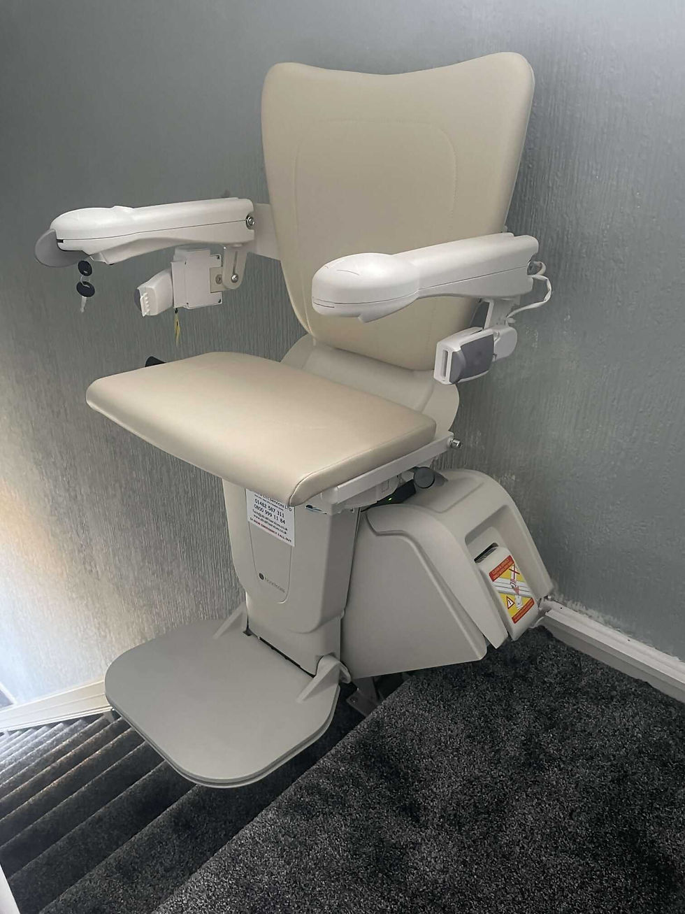 Close-up of a modern cream-colored stairlift chair with armrests and a footplate on a staircase.