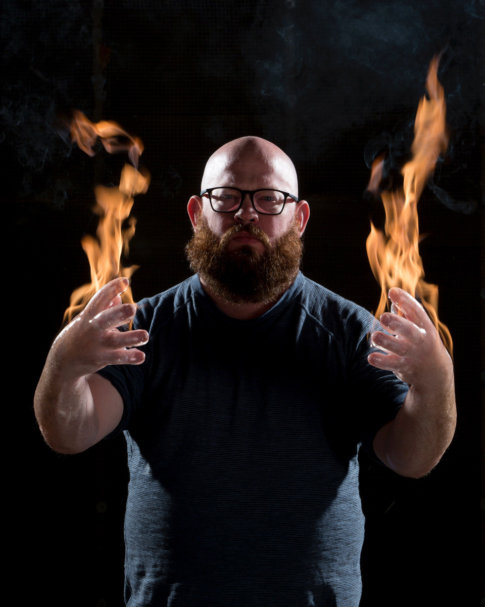 Picture of a bearded man with glasses, with fire rising from his palms