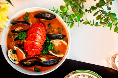 Image of a bowl of red stew filled with lobster tail, scallops and clams