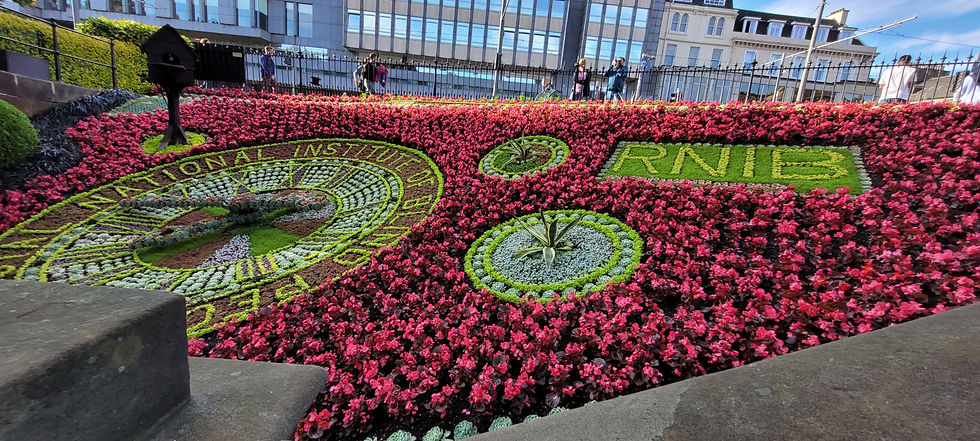 Intricate floral clock display surrounded by red flowers in Princes Street Gardens