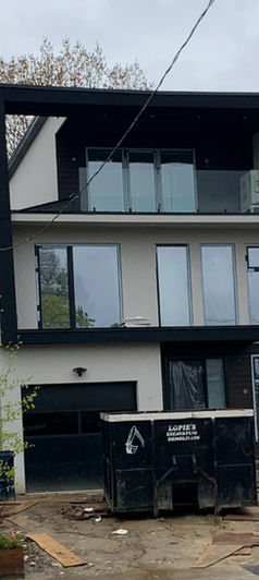 Modern custom home under construction with large windows, balcony framing, and exterior work in progress.