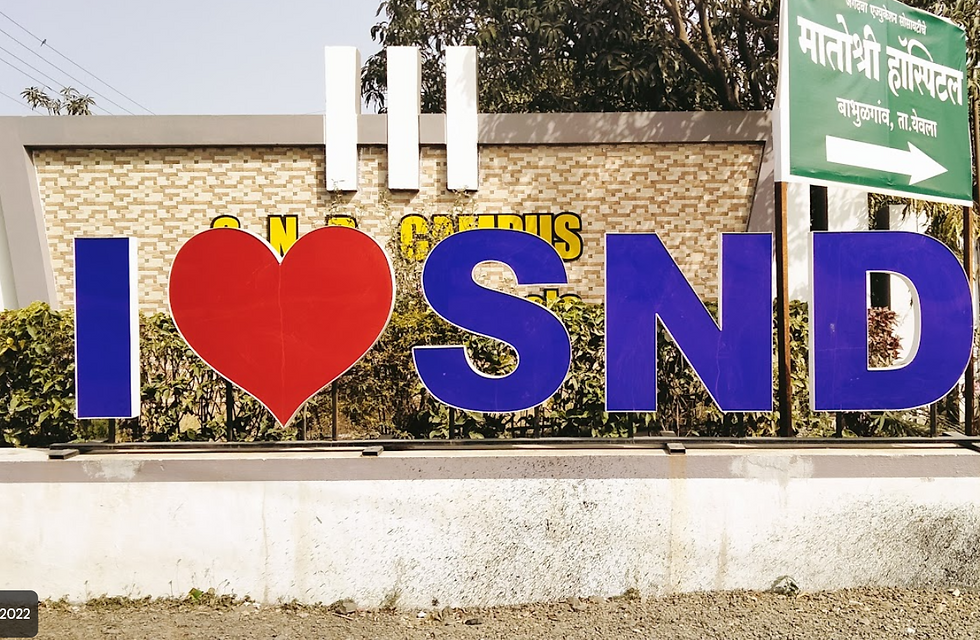 "I ❤️ SND" sign with a red heart and blue letters in front of a brick wall. Green foliage in the background, text on the wall partially visible.