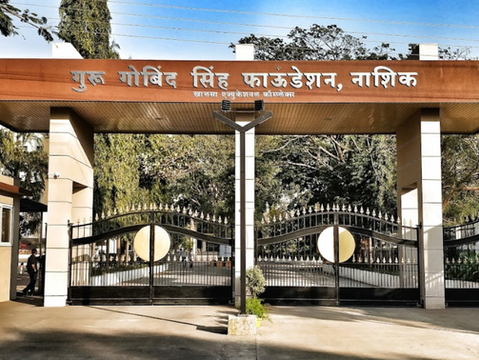 Entrance gate of Guru Gobind Singh Foundation, Nashik. Features black iron gates, a brown sign with text in Hindi, and greenery around.