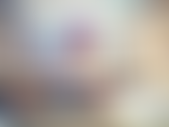 Crowd gathers in a courtyard with white buildings adorned with orange flags. A large banner displays text in a festive atmosphere.