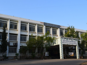 White multi-story academic building under a clear blue sky. Signs read "Main Academic & Administrative Building" in English and another language.