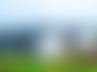 Aerial view of a large white building in a lush green landscape, under a cloudy sky. People walk along paths, and a few are near the entrance.