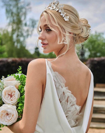 Messy bridal bun style with flower crown and face framing on blonde bride.