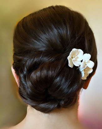 Bride with long brown hair in a sleek bridal bun with a flower pin attached on the side