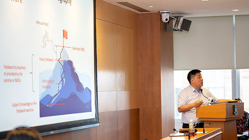 Man speaking at a podium in a conference room, beside a projected slide on fieldwork and inquiry framework.
