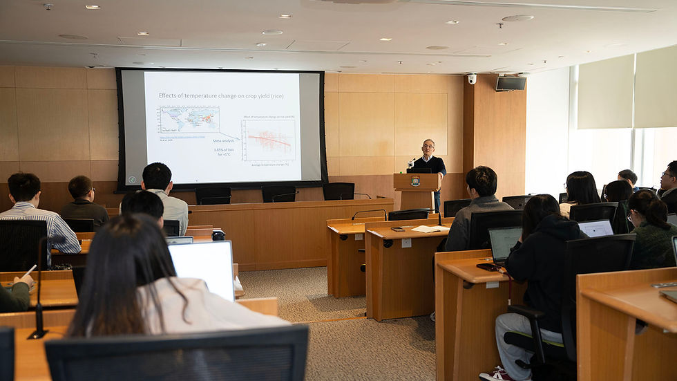 University lecture with a speaker at a podium presenting a slide on effects of temperature change on rice crop yield to seated students