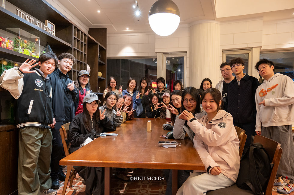 Group of students posing and smiling around a wooden table in a cozy restaurant, many making peace signs; HKU MChDS watermark visible.