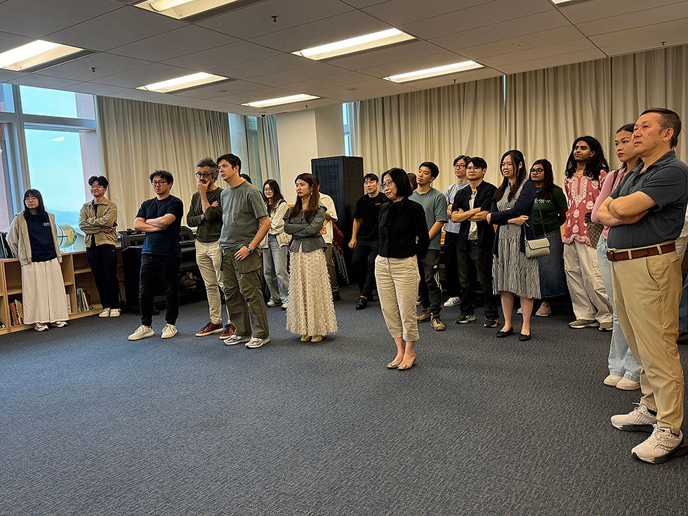 Group of adults stand listening in a meeting room with curtained windows and carpet, arms crossed, looking attentive and serious