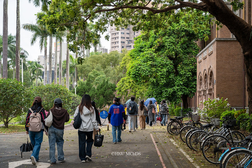 Students walk along a leafy campus path past parked bikes and a brick building; calm, overcast scene with HKU MChDS watermark